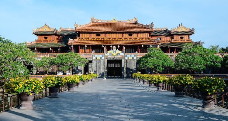 Grand gate of Hue's Imperial Citadel framed by flowering yellow shrubs and blue sky.