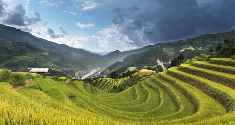 Sweeping view of green terraced rice fields curving down a mountain valley under dramatic clouds.