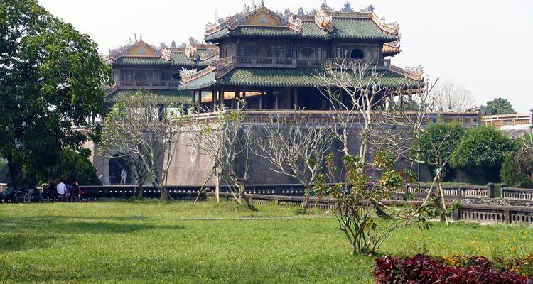 Historic royal palace with ornate roofs and moat set behind a grassy courtyard.