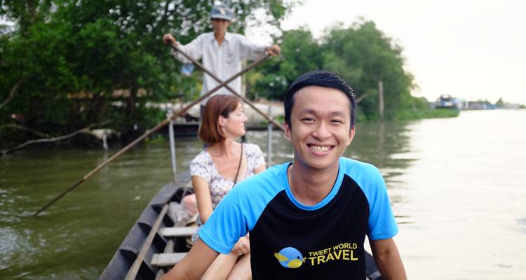 Smiling young man sits at the bow of a narrow wooden boat as it glides along a calm river.