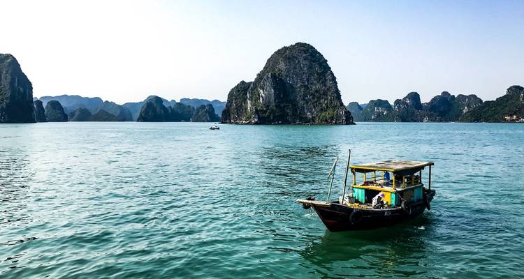 Ein hölzernes Dschunkenboot schwebt auf den smaragdgrünen Gewässern der Ha-Long-Bucht zwischen Kalksteinkegeln.