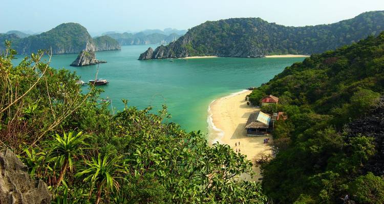 Secluded sandy beach and turquoise bay surrounded by forested limestone islands and lush greenery.