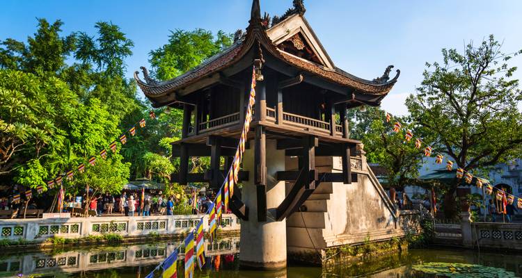 The iconic One Pillar Pagoda stands above a lotus pond with colorful prayer flags and visitors exploring the site.