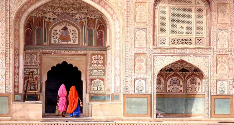 Zwei Frauen in traditioneller bunter Kleidung betreten einen geschmückten Palast.