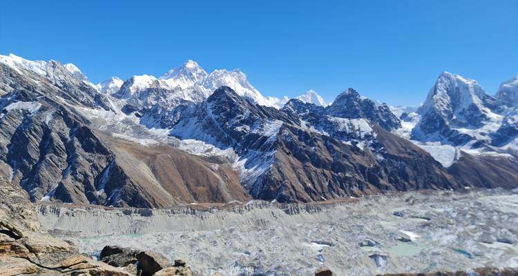 Vista amplia de un enorme glaciar gris con picos nevados dentados bajo un cielo azul brillante.