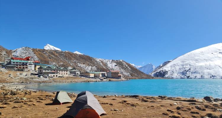 Lago de un turquesa brillante junto a un pueblo de piedra y carpas en gran altitud bajo un cielo sin nubes.