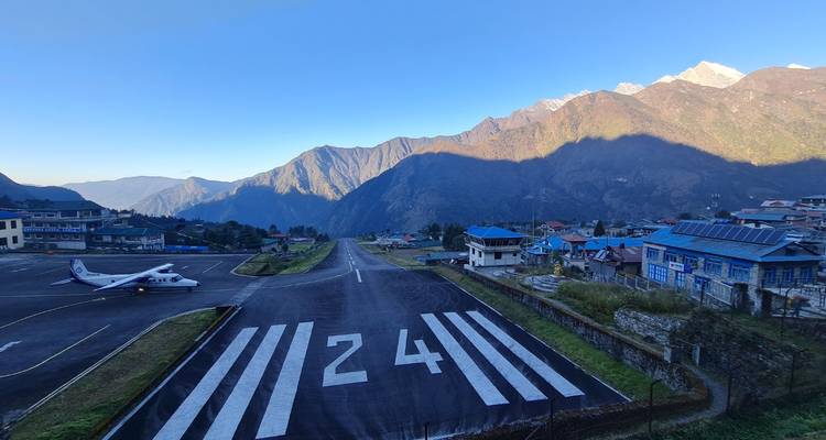 Pista 24 en el aeropuerto de Lukla con un pequeño avión de hélice estacionado y crestas montañosas rodeando el pueblo.