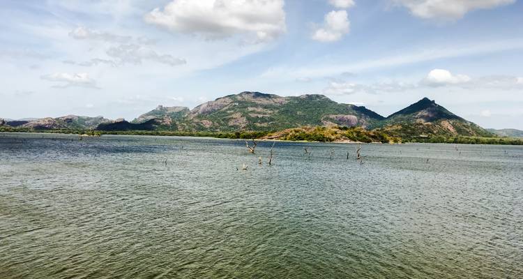 Un lac serein sous un ciel avec des nuages épars et des montagnes au loin.