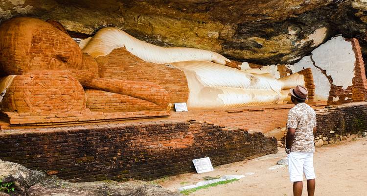 Une statue de Bouddha couché dans une grotte avec un homme qui l'observe.