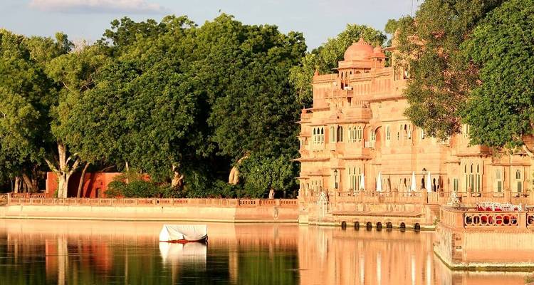 Palastartiges Gebäude mit Bäumen und einem Boot auf dem Wasser.