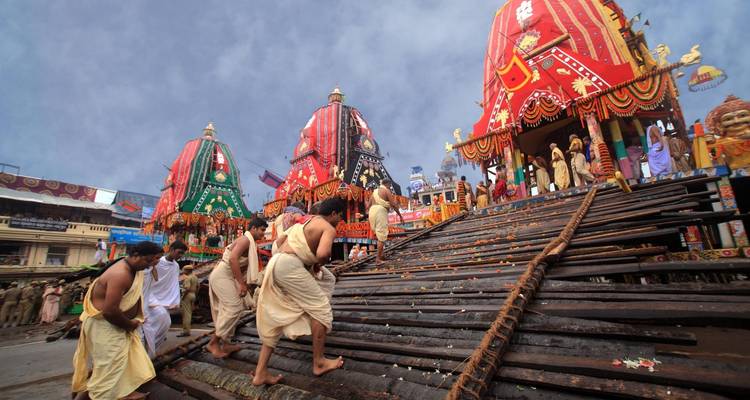 Men performing rituals in front of decorated chariots.