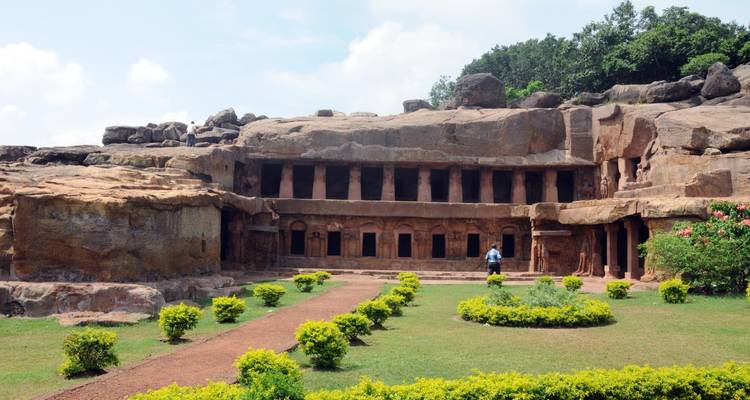 Cave complex with carved pillars and a gardened pathway.