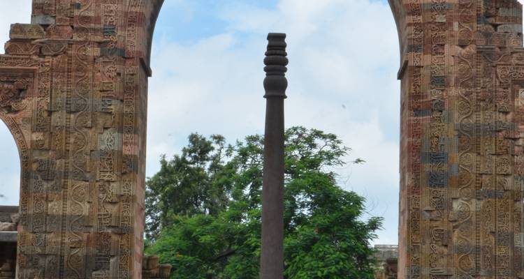 Kunstvolle Säule umgeben von antiken Ruinen und Bäumen.