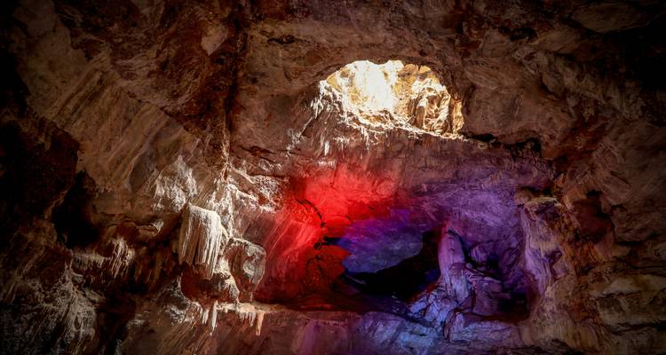 Cave ceiling with a natural opening and colorful lighting.
