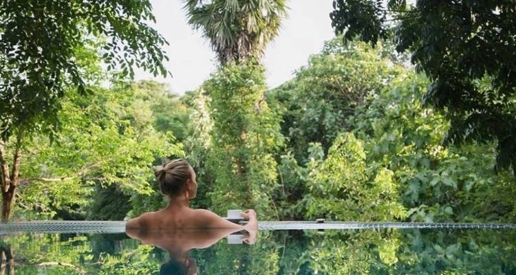 Person entspannt in einem Pool, umgeben von üppigem Grün.