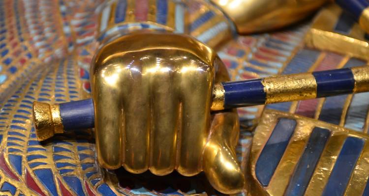 Een close-up van een gouden hand die een blauwe en gouden staf vasthoudt.