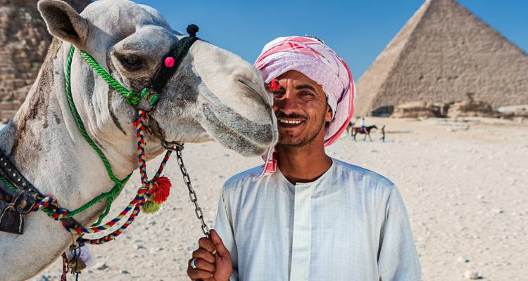 Een glimlachende man en een kameel met de piramide op de achtergrond.