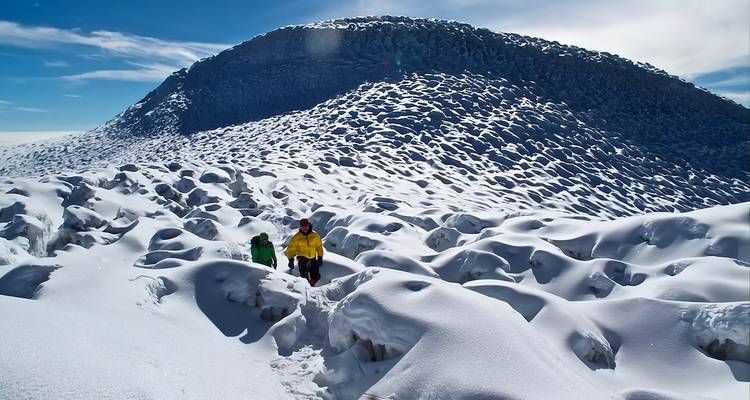 Des randonneurs traversent un champ de neige surréaliste aux crêtes sculptées par le vent sous le sommet glacé du Chimborazo.