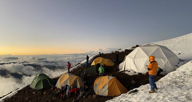 Des tentes d'expédition colorées parsèment une crête enneigée à l'heure dorée en altitude sur le Chimborazo, les nuages tourbillonnant en contrebas.