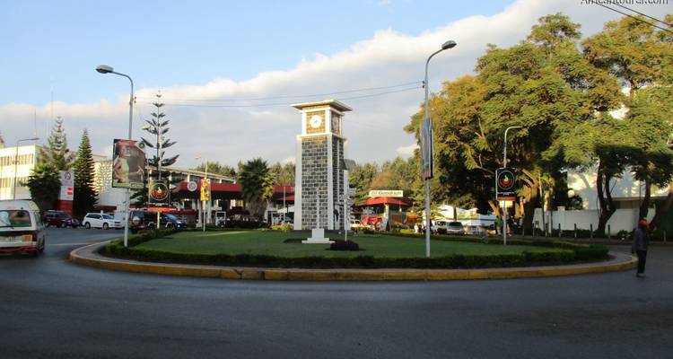Clock tower in a city roundabout with buildings around.