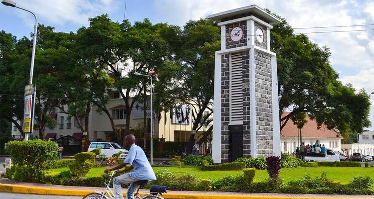 Man riding a bicycle past a clock tower in a city park.