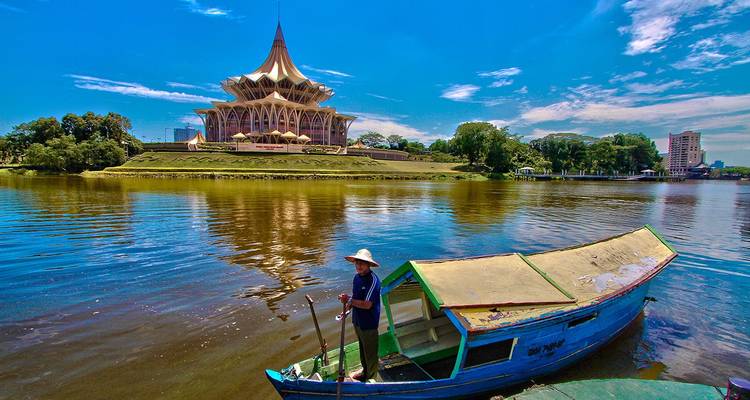 Boat on a river with an ornate building in the background under a clear sky.