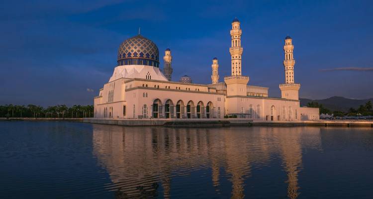 Kota Kinabalu City Mosque reflected in calm lagoon waters during blue hour.