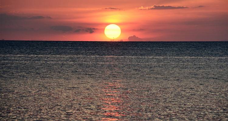 Le soleil d'un orange éclatant se couche à l'horizon, projetant des reflets sur une mer calme.