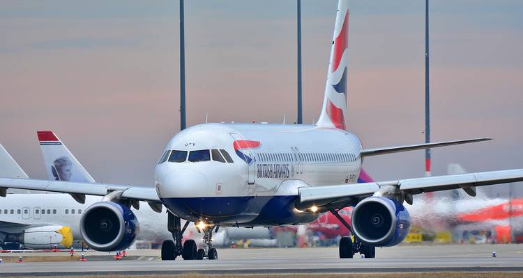 Een British Airways-vliegtuig taxiet tijdens het schemeren over een landingsbaan met andere toestellen op de achtergrond.