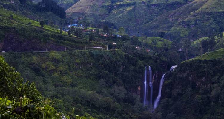 Wasserfälle umgeben von üppigem Grün und Bergen im Hintergrund.