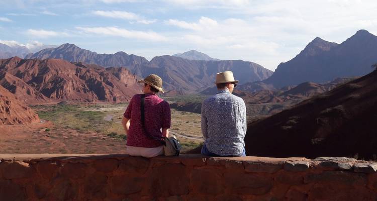 Paar sitzt auf einer Mauer und blickt auf ein Bergtal.