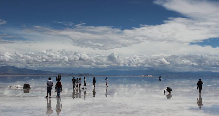 Eine Gruppe von Menschen, die auf einer ausgedehnten Salzebene wandelt, mit einem dramatischen Himmel und Bergen im Hintergrund.
