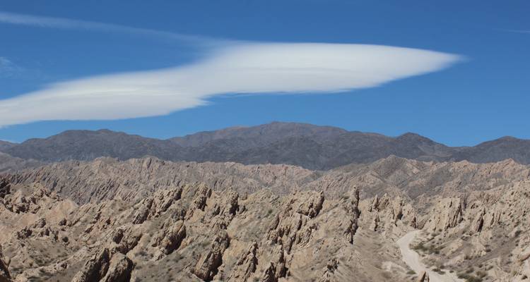 Raue und dramatische Felslandschaft mit einer markanten Wolkenformation in einem klaren blauen Himmel.