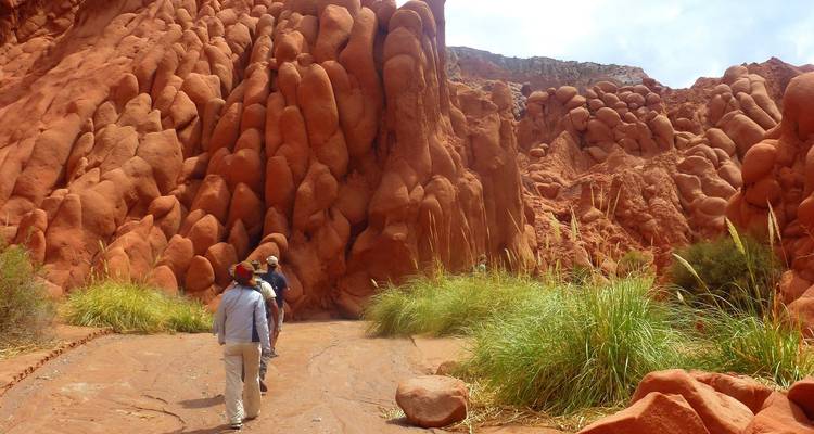 Wanderer, die zwischen roten Felsformationen in einer trockenen Landschaft gehen.