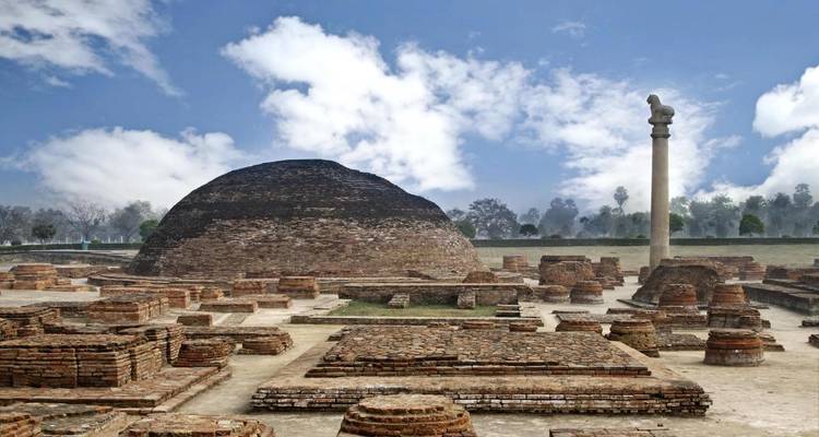 Ruines archéologiques de stupa en brique avec un pilier d'Ashoka solitaire sous un ciel bleu éclatant