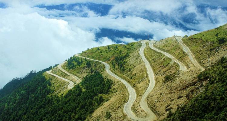 Kronkelende bergweg tussen bomen en wolken.