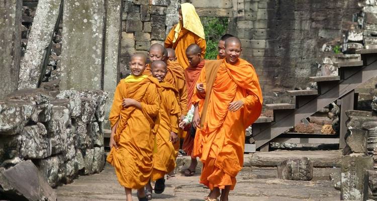 Grupo de jóvenes monjes con túnicas naranjas caminando por un sendero de piedra antigua.