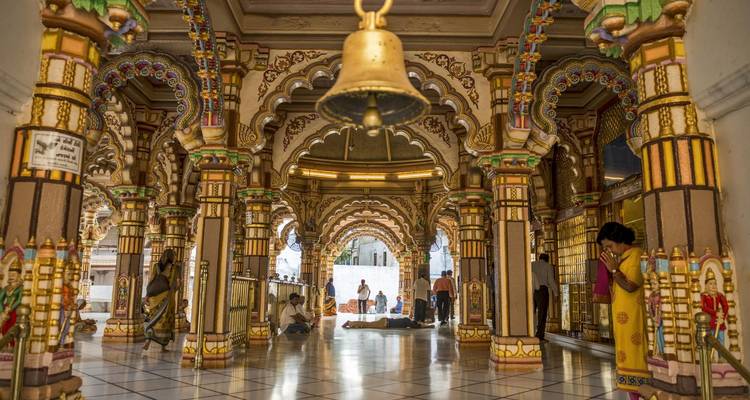 Wunderschön geschmückter Tempelinnenraum mit farbenfrohen Bögen und einer Glocke, Menschen in traditioneller Kleidung sind anwesend.