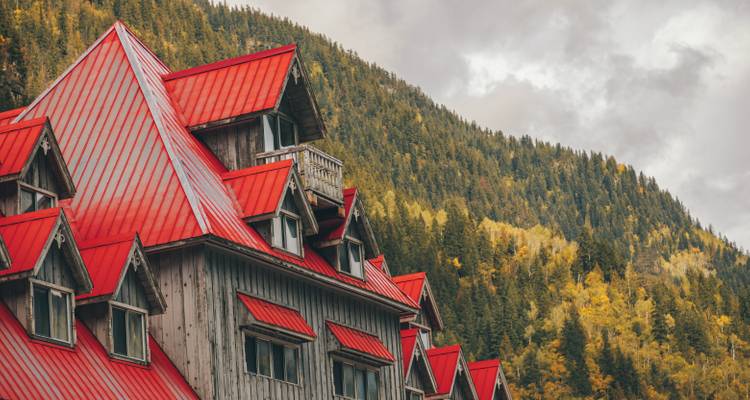 A rustic alpine lodge with bright red roofs nestled against a backdrop of forested mountains.
