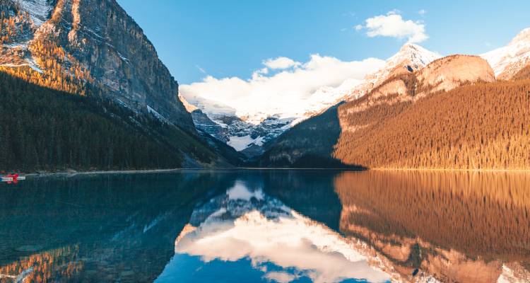 Crystal-clear lake mirroring towering snow-capped peaks and dense conifer forests in golden light.
