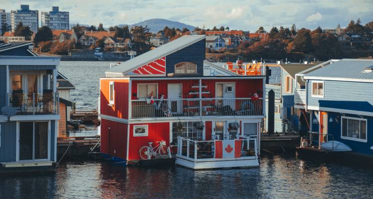 Floating colourful houseboats decorated with a Canadian flag docked along a calm harbour.