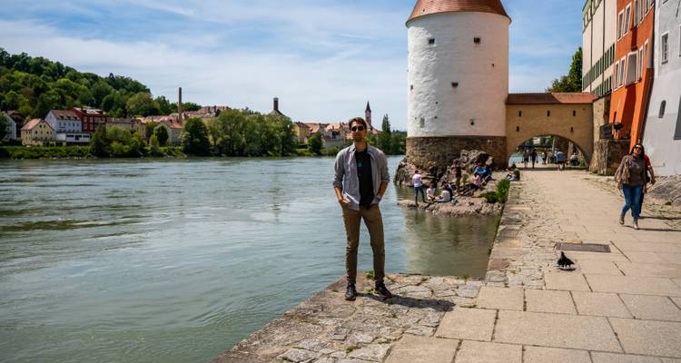 Voyageur debout sur une promenade en pierre le long d'une rivière, à côté d'une tour ronde et d'une rivière qui coule dans une ville historique.