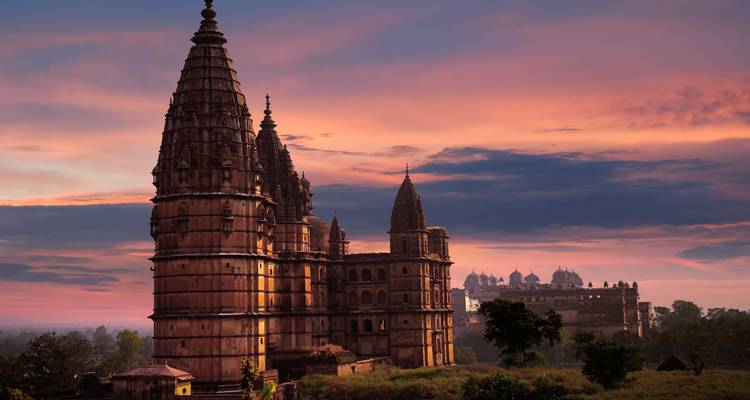 Medieval temple spires silhouetted against a dramatic pink and blue sunset sky.