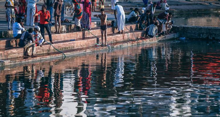 Locals perform ritual ablutions along stone steps beside a reflective holy pool.