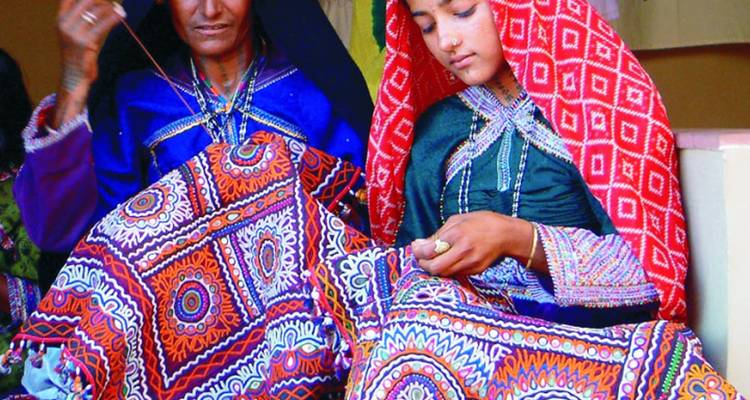 Zwei Frauen in traditioneller Kleidung arbeiten an Stoffstickerei.