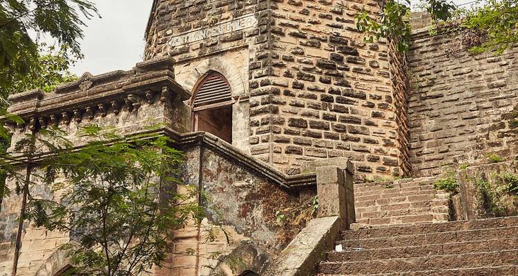 Old stone building with stairs leading up surrounded by trees.