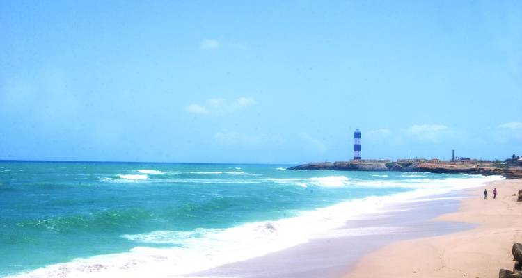 Küstenansicht mit Wellen und einem Leuchtturm in der Ferne.
