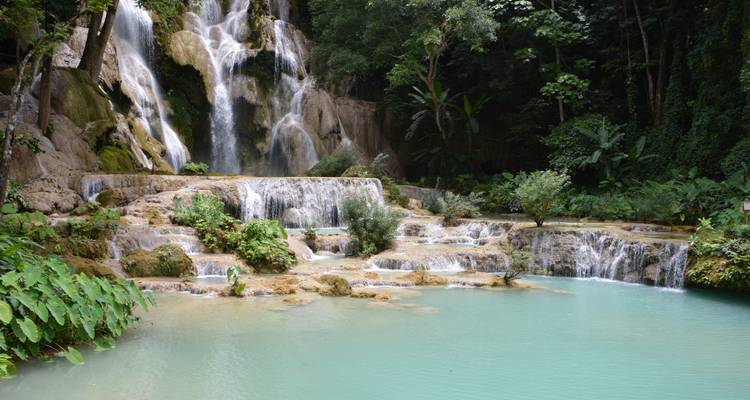 Une cascade à plusieurs niveaux se déversant dans un bassin turquoise entouré d'arbres.
