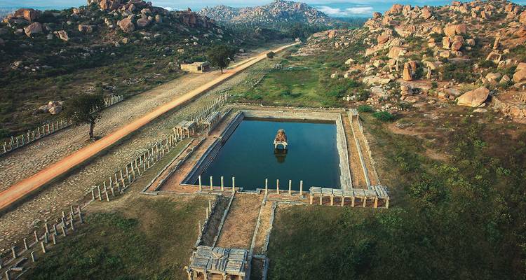 Lange antike Ruinen und Wasserreservoir inmitten felsigen Geländes.