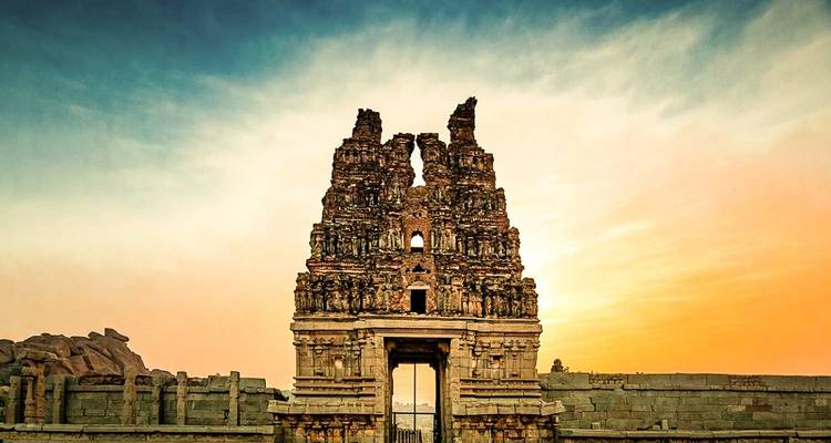 Ruins of a stone structure at sunset with a cloudy sky.